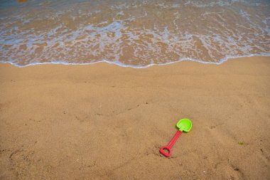 Yeşil bir plastik kürek kumun üzerinde yatıyor. Kürek sahilde, suyun yanında.