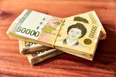 Tahta bir masada üç deste Kore banknotu. Para sarı ve üzerinde bir kadının yüzü var.