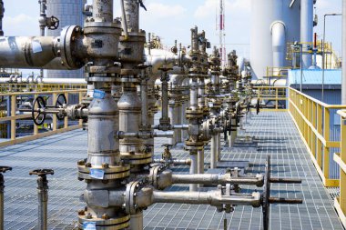 Kapakçık ve borular bir platformun üzerinde. Vanalar gümüş renkli ve üzerinde mavi etiketler var.