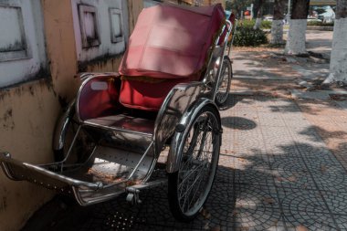 Gümüş çerçeveli kırmızı sandalye kaldırıma park edilmiştir. Sandalyenin kırmızı bir koltuğu ve kırmızı bir battaniyesi var.