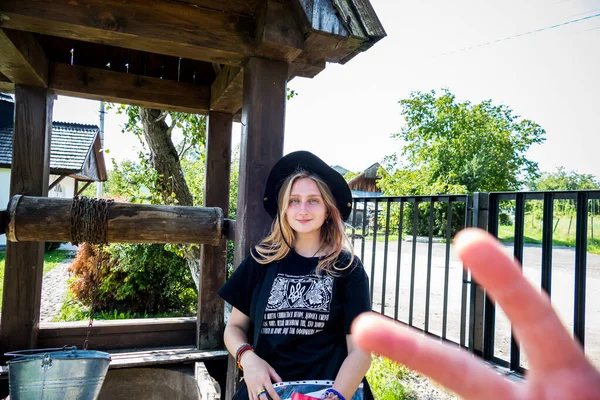 村の木の古い井戸の近くに黒の帽子と愛国的なTシャツの美しい女の子 — ストック写真