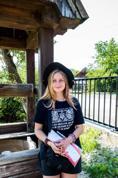村の木の古い井戸の近くに黒の帽子と愛国的なTシャツの美しい女の子 — ストック写真
