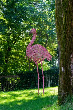 Pembe flamingo heykeli, telden örülmüş, yüksek bacaklar, çimenlerin üzerinde duruyor, park, ağaçların arasında, orijinal, şehir, yürüyüş, seyahat, manzara, doğa, gezinti, yaz, bahar, çocuk kampı, turistler, dinlenme, 