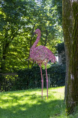 Pembe flamingo heykeli, telden örülmüş, yüksek bacaklar, çimenlerin üzerinde duruyor, park, ağaçların arasında, orijinal, şehir, yürüyüş, seyahat, manzara, doğa, gezinti, yaz, bahar, çocuk kampı, turistler, dinlenme, 
