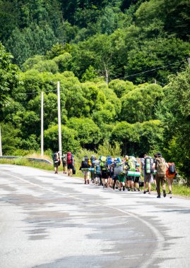 Çocuklar ve yetişkinler yol boyunca omuz çantaları, karyolalar, yürüyüş, gezi, yaz, gözcüler ile yürür.