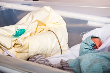 Küçük el, ön plan, yeni doğan, yeşil kukla, mavi beden, çizgili pantolon, hastane yatağı, desenli bebek bezi, beyaz yatak, makro, yakın plan, iç mekan.,