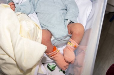 Bebek bezi, yeni doğan bacağı, turuncu çorap, mavi beden, anne eli, bilgi bileziği, filli bebek bezi, beyaz yatak, yakro, yakın plan, iç mekan, kadın, bakım, bebek