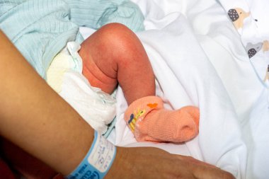Bebek bezi, yeni doğan bacağı, turuncu çorap, mavi beden, anne eli, bilgi bileziği, filli bebek bezi, beyaz yatak, yakro, yakın plan, iç mekan, kadın, bakım, bebek