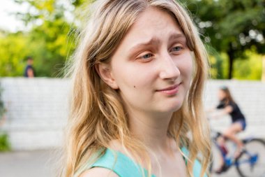 18 yaşında genç bir kadın, beyaz saçlı, gülümseyen, şaşırmış görünen, alnındaki kırışıklıklar, yanağındaki ben, yeşil gözlü, portre, yakın plan, yaz,