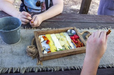 people tasting cheese slices, different types in wooden box, multi-colored, honey in a bowl, food, snack, tasty, sprig of spice, hands, burlap napkin, horizontal photo