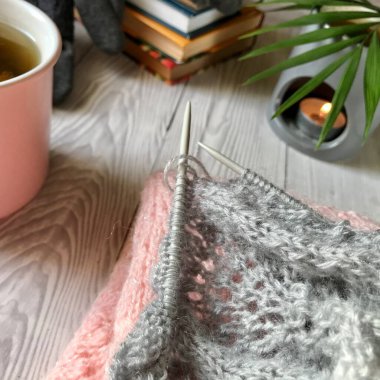 Gri arka planda, çiçek çayı örgünün yanında, ve kitapların yanında eldivenlerin uzandığı bir aroma mumu var.