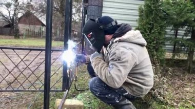 a masked welder is welding the iron structure of the gate
