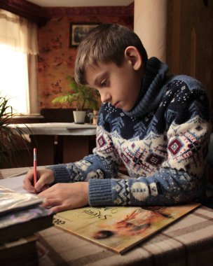 Noel süveteri giyen bir çocuk boş zamanlarında yazar ve çizer.