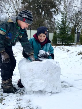 Yeşil ceketli bir çocuk kışın kardan adamın üzerine kar katmanları serer.