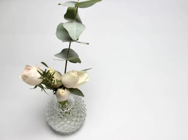 small round decorative vase with small flowers and a sprig of eucalyptus on a light background with space for text