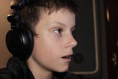 12 yaşında siyah cüppeli bir çocuk kulaklıkla bilgisayarın başına oturmuş internette oyun oynuyor..