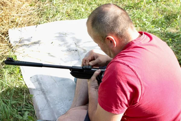 一个穿着红色T恤的男子坐着装上机关枪 学习如何射击和准备比赛 — 图库照片