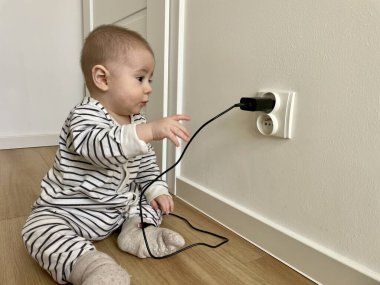 Çizgili elbiseli küçük bir çocuk odadaki prizlere tırmanıyor.