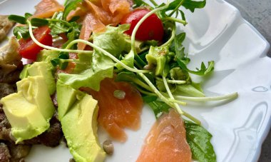 Beyaz bir tabakta - kiraz domatesli salata, yeşil roka, avokado, somon ve mantar parçaları. Yüksek kalite fotoğraf