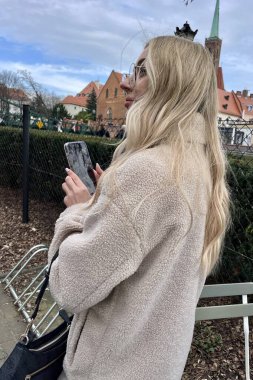 Gözlüklü, elinde telefon, parktaki bej ceketli güzel bir sarışın.