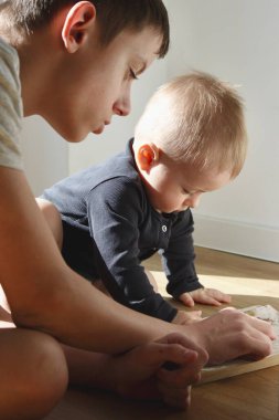 Bir genç, küçük kardeşine yeni yürümeye başlayan bir çocuğu bir kitabı göstererek öğretir..