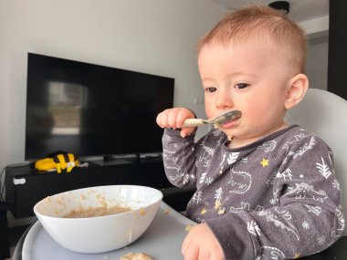 Bir çocuk kaşık yer ve yulaf lapası yer.