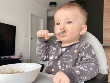 Küçük çocuk mutfakta bıçakla kaşık yiyor.