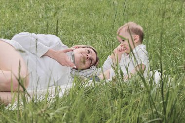 Küçük oğlu olan genç bir anne güneşli bir havada parktaki çayırda dinleniyor.