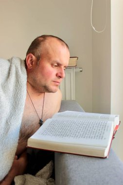 Bir adam kanepede uzanmış kitap okuyor.