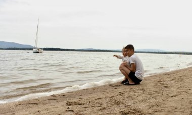 Büyük kardeş nehrin kıyısındaki küçük çocuğa, iki çocuğa nehri gösterir..