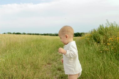 Çocuk tarlada duruyor ve bir şeye bakıyor.