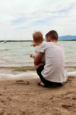 Büyük kardeş nehrin kıyısındaki küçük çocuğa, iki çocuğa nehri gösterir..