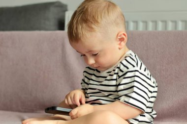 Kanepede oturan küçük bir çocuk telefona bakıyor.