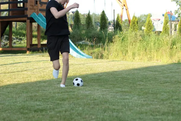 Bir genç, yeşil çimlerin üzerinde beyaz çoraplarla, yalın ayakla top oynuyor..