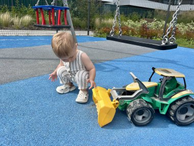 Küçük bir çocuk oyun alanında büyük bir oyuncak traktörle oynuyor.