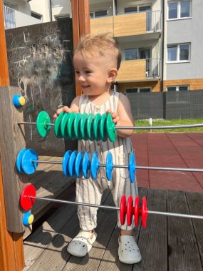 Küçük bir çocuk oyun bahçesinde renkli bir abaküs ile öğrenirken eğleniyor..