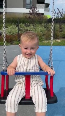 Küçük bir çocuk salıncakta sallanarak ve gülerek eğleniyor.