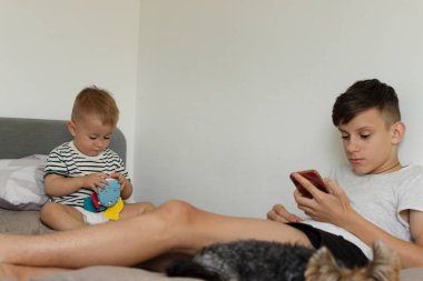 Genç bir kız telefonuyla oturuyor, yanında da bir köpek ve küçük bir kardeş oturuyor.