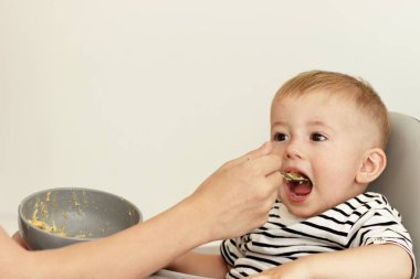 Küçük bir çocuğu kaşıkla lapayla besleyen bir el.