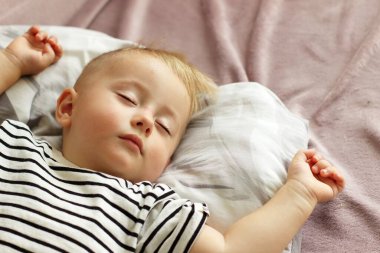 Küçük bir çocuk kapalı gözlerle uyur, bir bebek gündüz uyur.