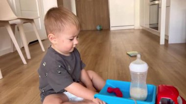 Küçük bir çocuk oynuyor, oyuncak bir arabada bir şişe süt taşıyor.