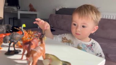 Oyuncak hayvanlarla oynayan küçük bir çocuk, ağzında küçük bir parça alır ve bir yetişkin tehlikeyi engeller.