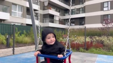 Sonbahar kıyafetleri giymiş küçük bir çocuk oyun parkında sallanıyor.