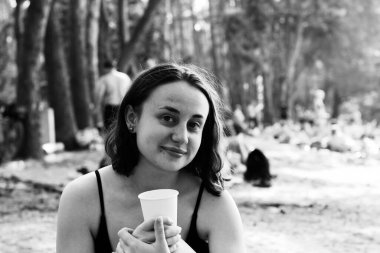 Elinde bardakla hafta sonu doğada dinlenen neşeli bir kızın siyah beyaz portresi.