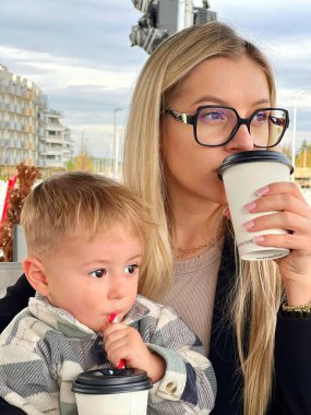 Bir anne ve bir çocuk bir kafede içki içiyorlar. Bardaklı genç bir kadın kahve içer, bir bebek kollarına oturur ve tüple süt içer..