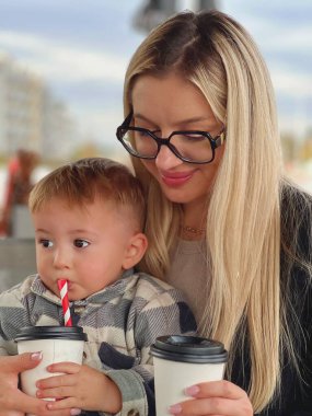 Bir anne ve bir çocuk bir kafede içki içiyorlar. Bardaklı genç bir kadın kahve içer, bir bebek kollarına oturur ve tüple süt içer..