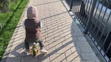 Bir çocuk mobilete biniyor. Küçük bir çocuk, sıcacık giyinmiş, yol boyunca bir kros bisikleti sürüyor.