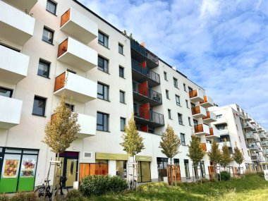 Turuncu balkonlu, genç ağaçların diktiği beyaz bir kasaba evi.