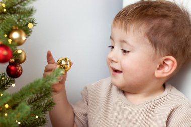 Küçük bir çocuk yeşil bir yılbaşı ağacındaki yeni yıl süslemelerine bakıyor. Yüksek kalite fotoğraf