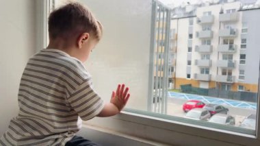 Küçük bir çocuk oturur ve pencereden sokağa bakar.